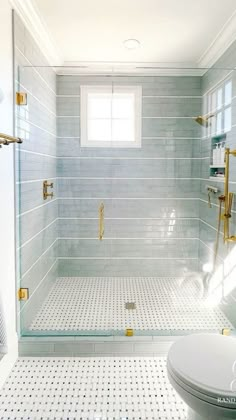 a bathroom with white and gold fixtures, glass shower doors, and tile flooring