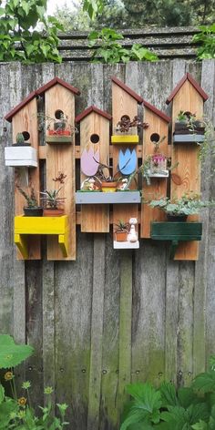 several birdhouses are hanging on the side of a wooden fence with plants in them