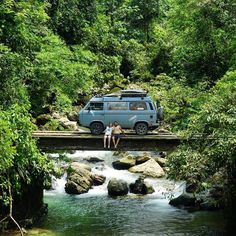 two people are standing on a bridge over a river with a van in the background