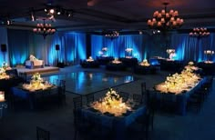 an empty ballroom with blue drapes and chandeliers on the ceiling is lit by candles