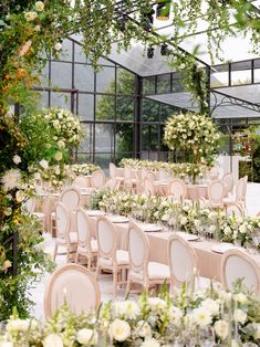 tables and chairs are set up for a formal function in a glass walled area with greenery