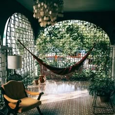 a hammock hanging in the middle of a room with two chairs and a chandelier