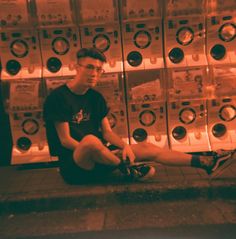 a young man sitting on the ground in front of stacks of washing machine's