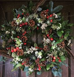 a christmas wreath with berries, pine cones and evergreens on a wooden door frame