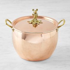 a large metal pot with gold handles on a marble counter top, holding a small golden leaf ornament