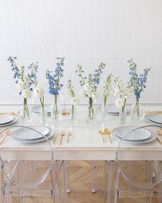 the table is set with plates, silverware and vases filled with blue and white flowers