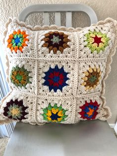 a crocheted pillow is sitting on a chair with a white back and sides