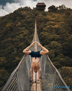 a man standing on a suspension bridge with his hands in the air and looking down