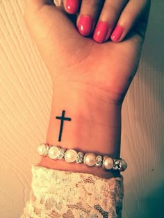 a woman's wrist with a cross tattoo on it and pearls around the wrist