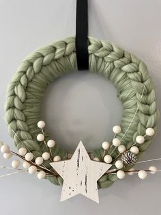 a green wreath hanging on the wall with white balls and pineconis attached to it