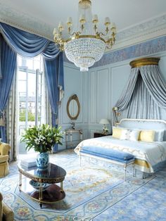 a bedroom with blue and gold decor, chandelier, bed, couch, chair, coffee table