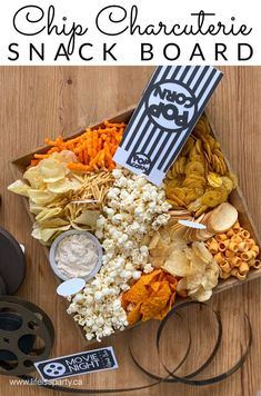 a box filled with chips and snacks on top of a wooden table next to a movie reel