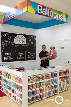 a man holding a stuffed animal in front of a store counter with balloons on it