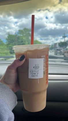 a woman holding up a cup of coffee in the back seat of a car with a sticker on it