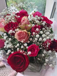 a bouquet of red and pink roses in a vase on a window sill with white baby's breath