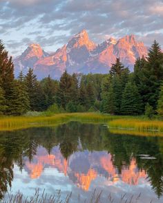 a mountain range is reflected in the still water of a lake with trees around it