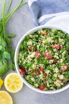 a white bowl filled with salad next to lemons and cilantro on a gray surface