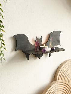 a bat shaped candle holder is mounted on the wall next to a vase with candles in it