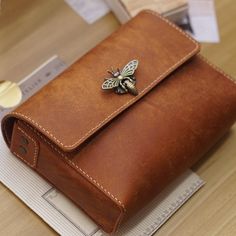 a brown leather wallet with a bee on the front and side pocket, sitting on top of a desk