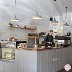 a woman standing behind a counter in a restaurant with lights hanging from the ceiling above