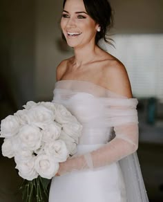 a woman in a white dress holding a bouquet of flowers on her left hand and smiling at the camera