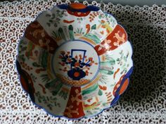 a decorative bowl is sitting on a lace tablecloth with an orange and blue design