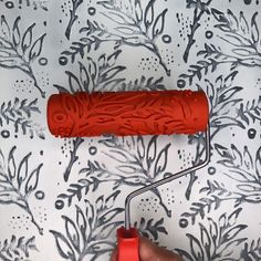 a person holding a paint roller in front of a wallpapered background with black and white designs