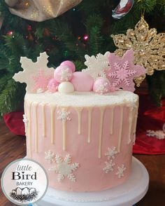 a pink frosted cake sitting on top of a table next to a christmas tree