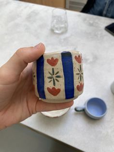 a hand holding a small cup with hearts painted on the outside and inside, in front of a white table