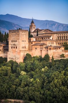 an old castle with trees and mountains in the background