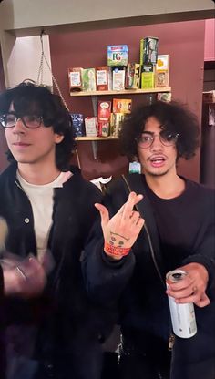 two young men standing next to each other in front of a shelf with books on it