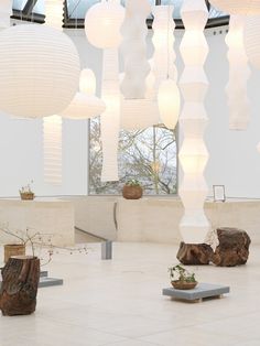 the room is decorated with white paper lanterns and wood stumps as well as plants