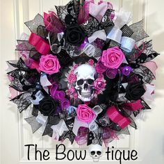 the bowtiquee wreath is decorated with pink and black roses, skulls and ribbons