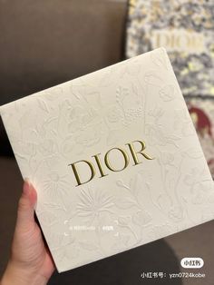 a person holding up a white box with the word dior on it in gold lettering