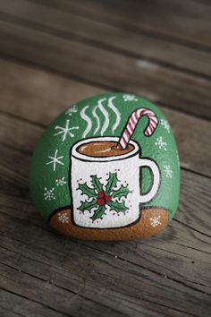 a painted rock with a cup of hot chocolate and candy cane sitting on top of it