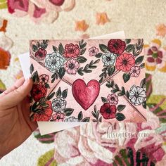 a hand holding up two cards with flowers on them and a heart in the middle