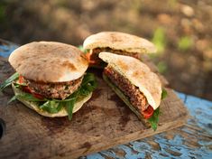 two hamburgers sitting on top of a wooden cutting board