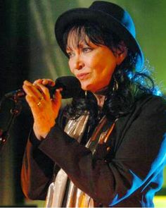 a woman wearing a black hat and holding a microphone in her right hand while standing on stage