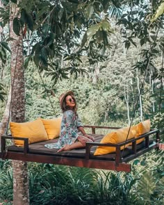 a woman sitting on top of a wooden platform in the middle of a forest with yellow pillows