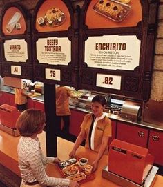 two people sitting at a counter in a fast food restaurant with signs on the wall