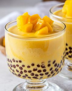 two glasses filled with pudding and topped with mango slices on the top one glass is half full