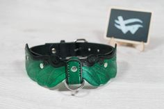 a green leather dog collar with leaves on it and a small black square sign in the background