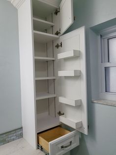 an open cabinet in the corner of a room with white walls and drawers on both sides