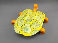 a skateboard shaped like a turtle sitting on top of a gray surface with yellow wheels