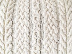 a white knitted blanket with cables on it