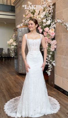 a woman standing in front of a flower display wearing a wedding dress with an open back