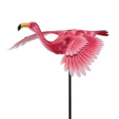 a pink flamingo standing on top of a metal pole with its wings spread out