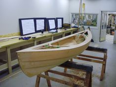 a wooden boat sitting on top of a table next to two monitors and some shelves