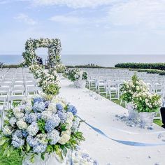 an outdoor ceremony setup with blue and white flowers on the aisle, overlooking the ocean