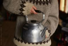 a person holding a metal tea kettle with a cat design on the top and handle